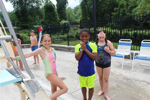 Three kids standing by pool ladder