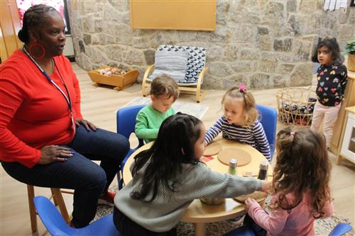 Woman sits at table with young students