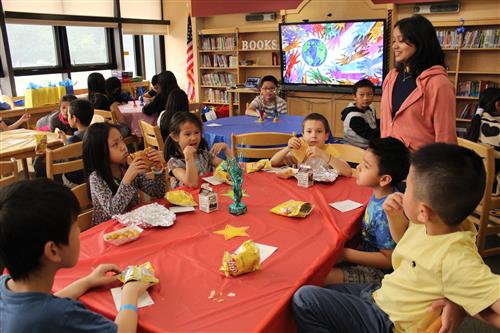 Group of students seated at table while women, standing, speaks to them