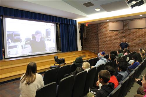 Man on screen talking to students seated in an auditorium