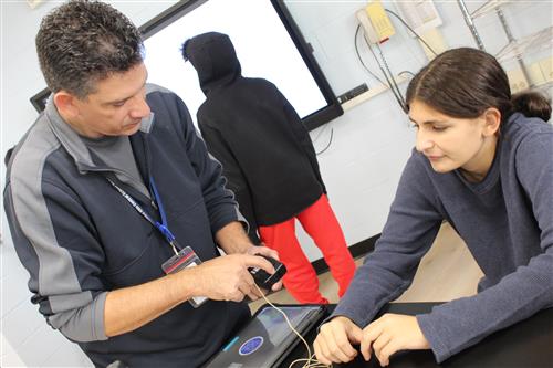 Girl sits at desk while man helps with project